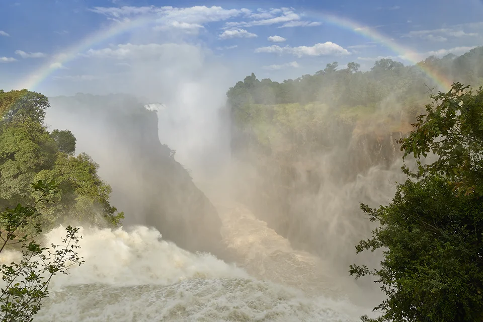 Rainbow forming over the mist-filled gorge of Victoria Falls on the Zambezi River
