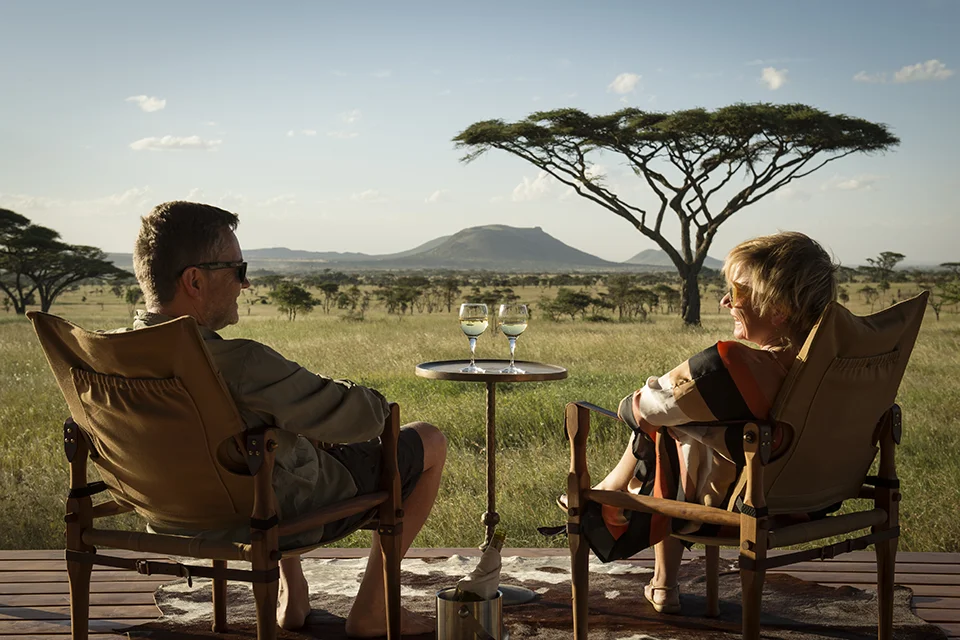 Couple enjoying sundowners with views across the Serengeti plains at sunset, Tanzania