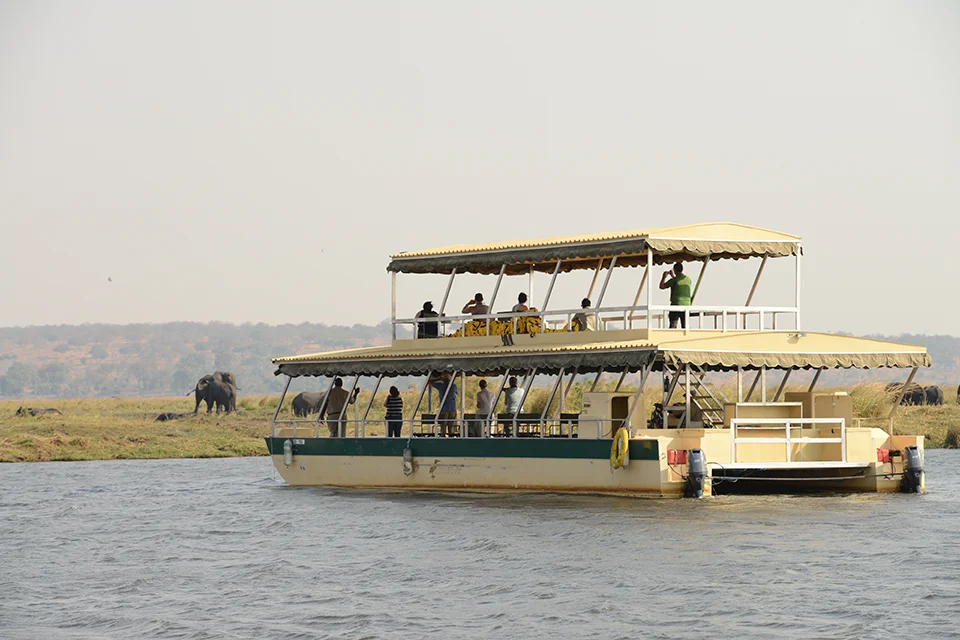 Guests aboard a double-deck safari boat watch elephants along the banks of the Chobe River in Chobe National Park, Botswana