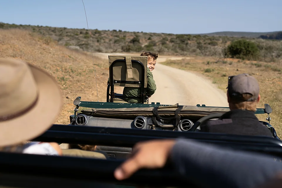 A smiling child looks back at the family while riding at the front of a safari vehicle