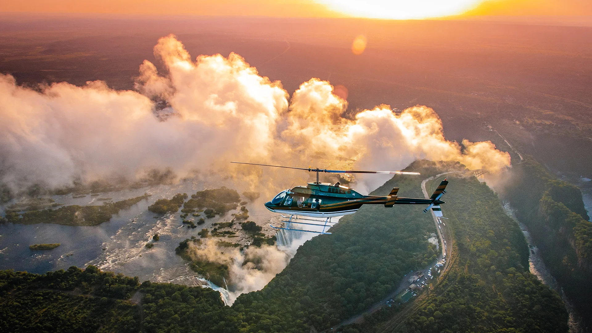 Helicopter flying above Victoria Falls at sunrise, with mist rising from the Zambezi River gorge in Zimbabwe and Zambia