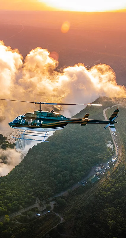 Helicopter flying above Victoria Falls at sunrise, with mist rising from the Zambezi River gorge in Zimbabwe and Zambia