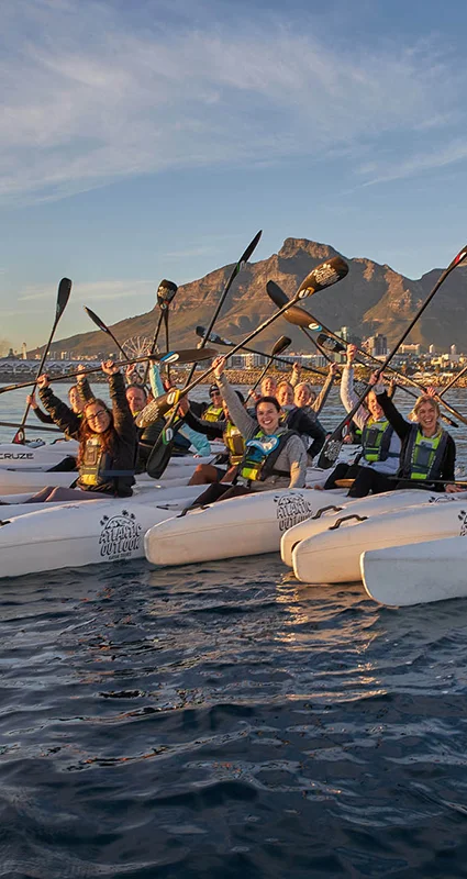 Group of kayakers raising their paddles with Table Mountain in the background, Cape Town