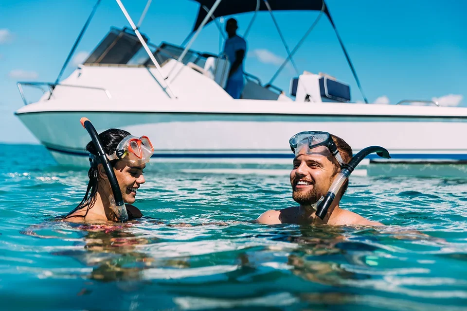 Travellers wearing snorkelling masks and snorkels floating in clear turquoise water beside a boat