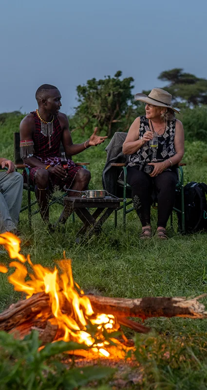 Guest chatting with a Maasai guide beside a campfire at Tawi Lodge near Amboseli National Park, Kenya
