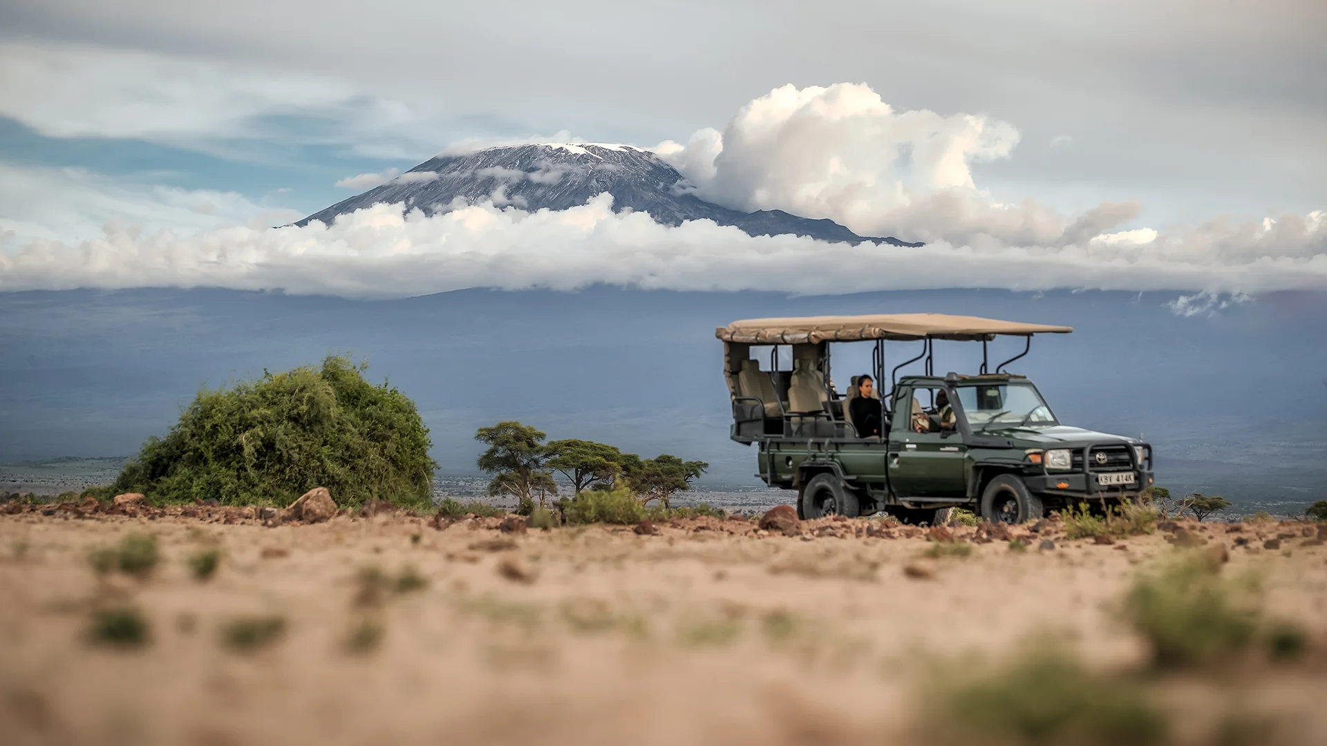 Safari vehicle on the Amboseli plains with Mount Kilimanjaro rising above the clouds in the background