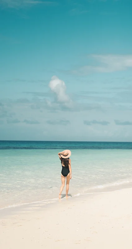 Woman walking along a white-sand beach beside turquoise waters in Zanzibar, Tanzania